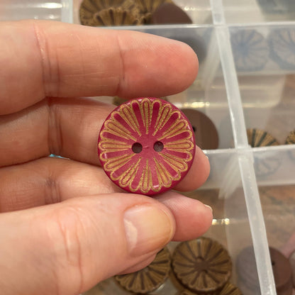 Hand holding a pink floral button with a clear container of assorted buttons in the background