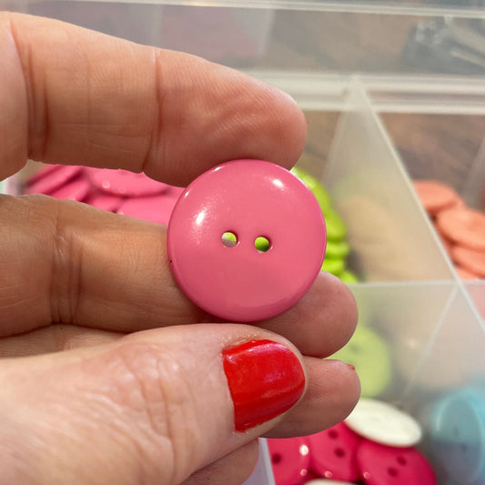 Hand holding a pink button with a container of colorful buttons in the background