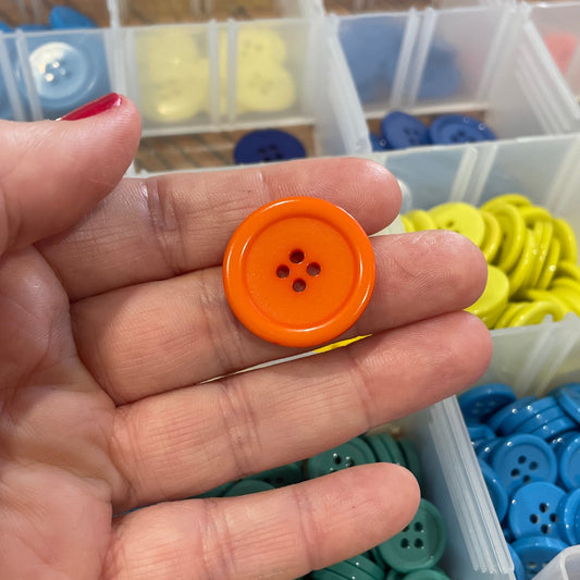 Hand holding an orange button with a container of assorted buttons in the background