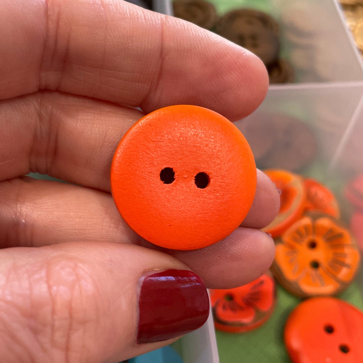 Hand holding an orange button with a container of colorful buttons in the background