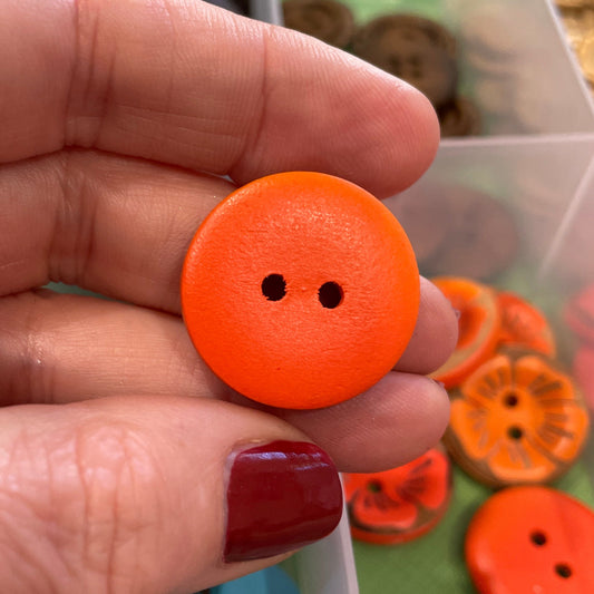 Hand holding an orange button with a container of colorful buttons in the background
