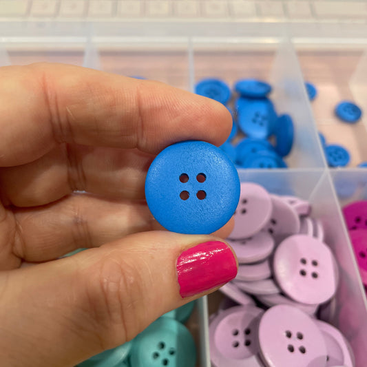 Hand holding a blue button with a container of colorful buttons in the background