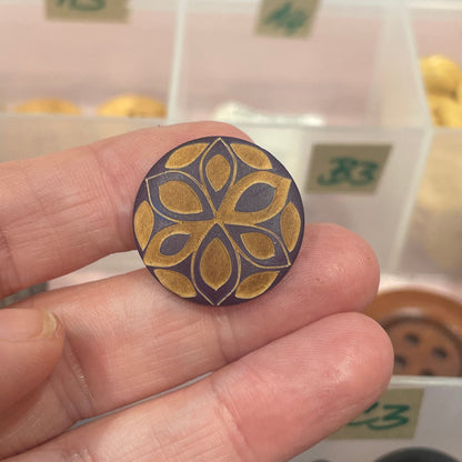 Hand holding a decorative button with a floral design, surrounded by various buttons in the background.