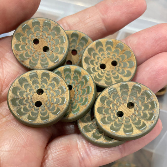 Hand holding a collection of green ceramic buttons with intricate patterns.