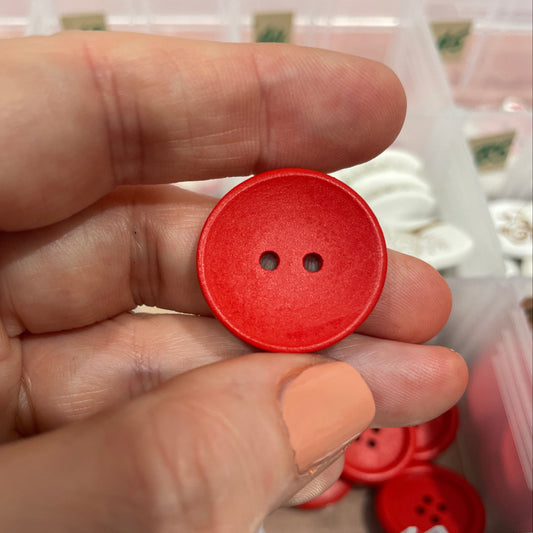 Red button held between fingers with sewing materials in the background