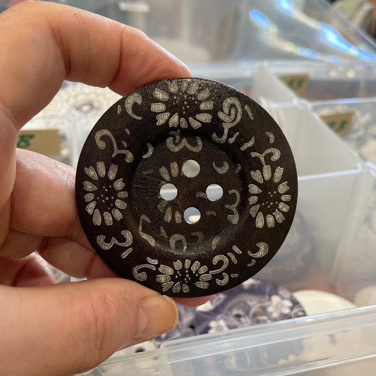 Hand holding a decorative black and white circular object with intricate patterns in a blurred indoor setting.