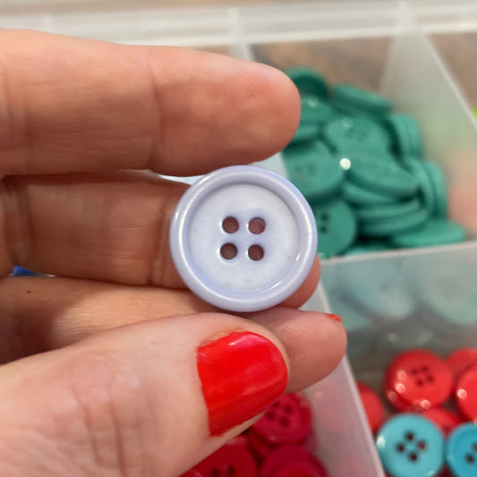Hand holding a white button with a container of colorful buttons in the background