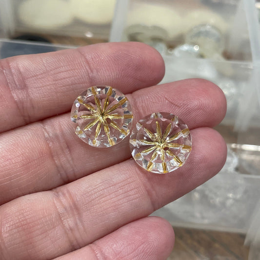 Two round cut gemstones held between fingers with a clear jewelry box in the background.