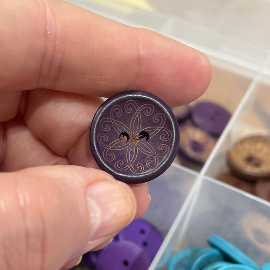 Hand holding a decorative button with a box of assorted buttons in the background