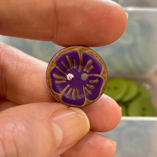 Hand holding a purple floral button with a container of buttons in the background