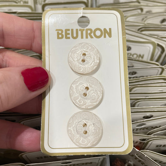 Three buttons on a BEUTRON card held by a hand with red nail polish.