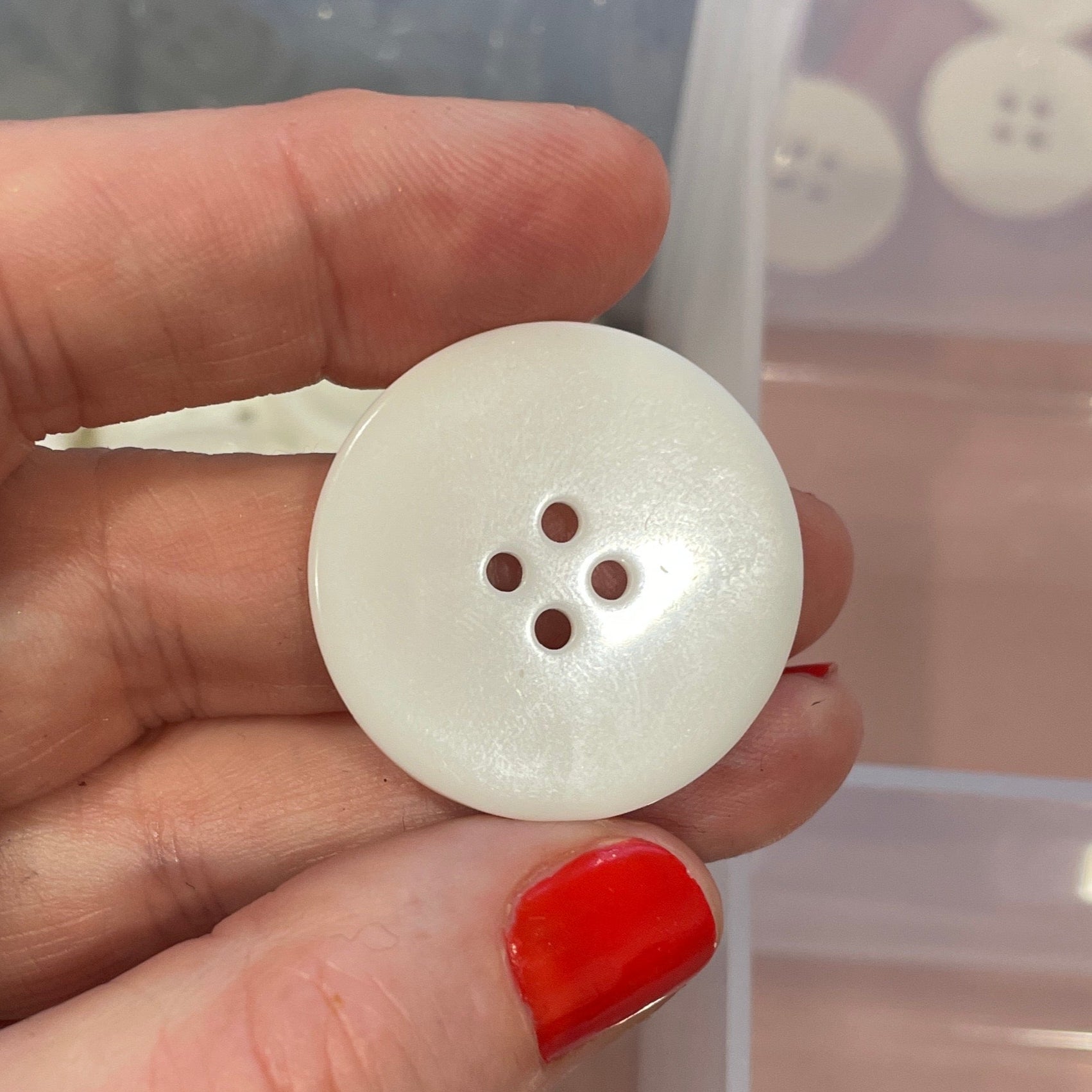 Hand holding a white button with a clear container of buttons in the background