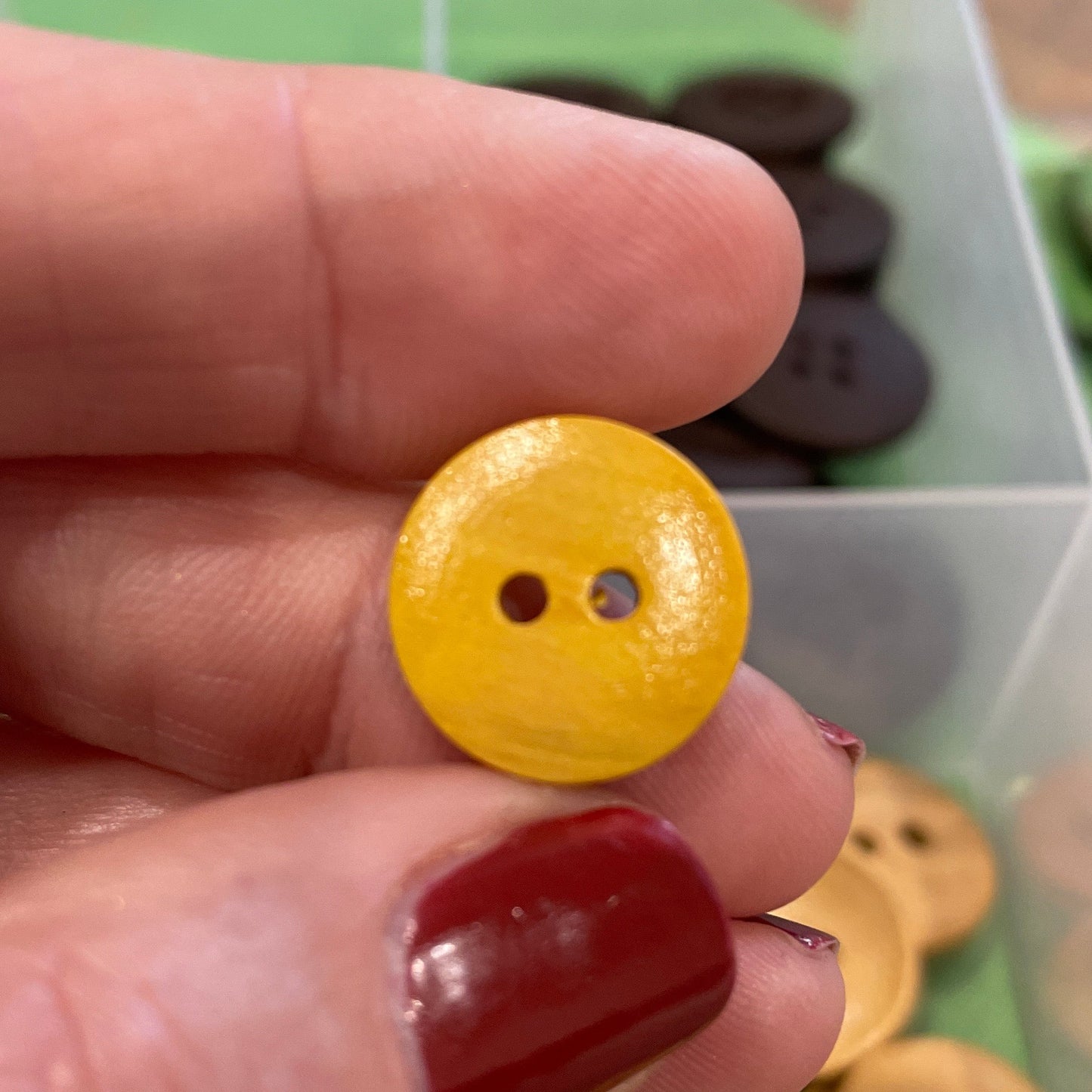 Hand holding a yellow button with a container of buttons in the background