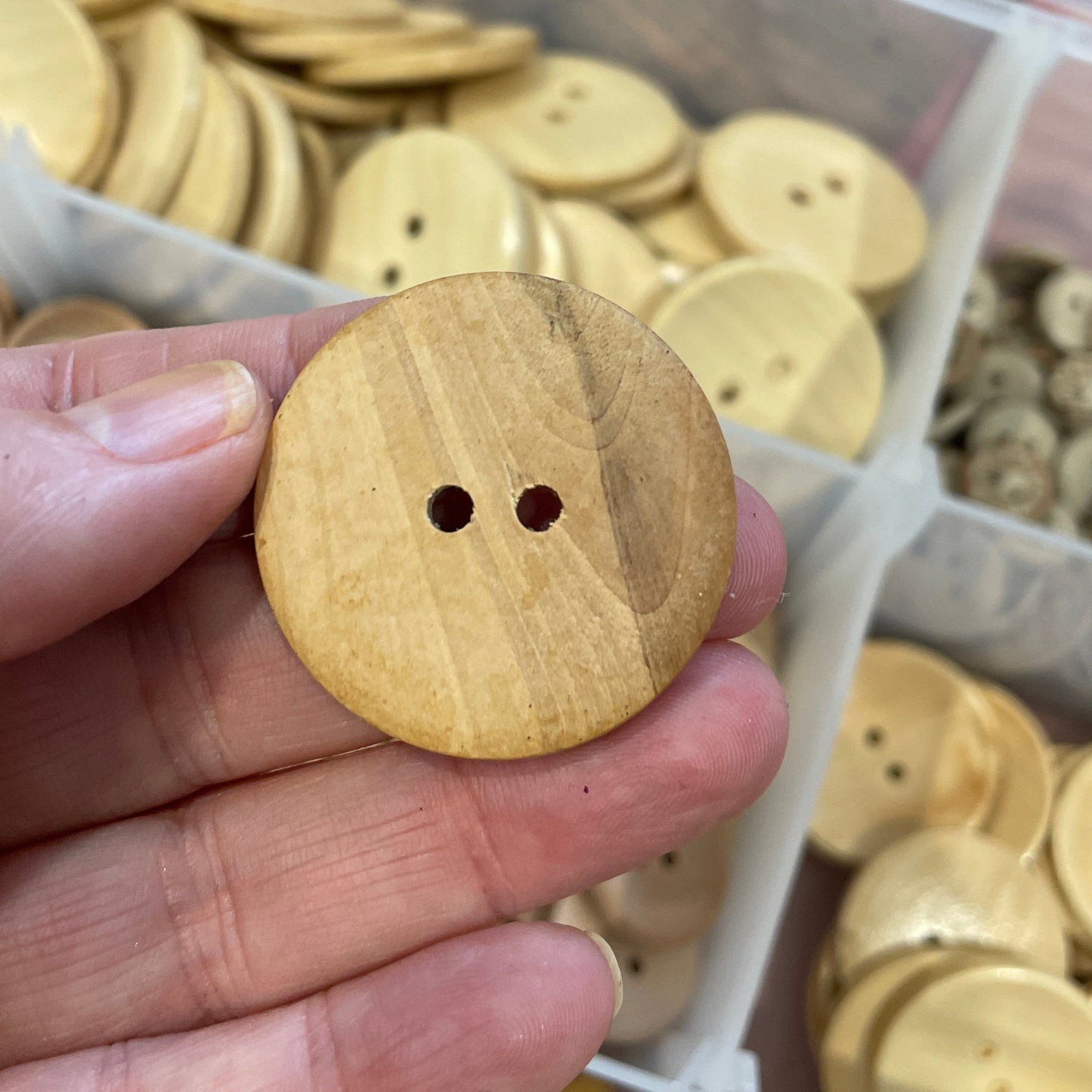 Hand holding a wooden button with a container of buttons in the background