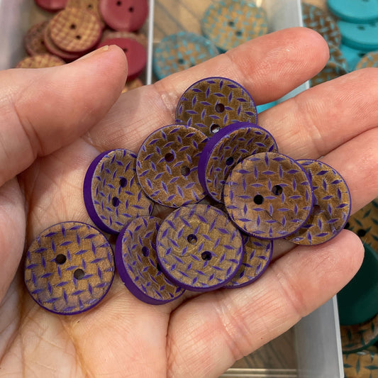 Hand holding purple buttons with a container of assorted buttons in the background