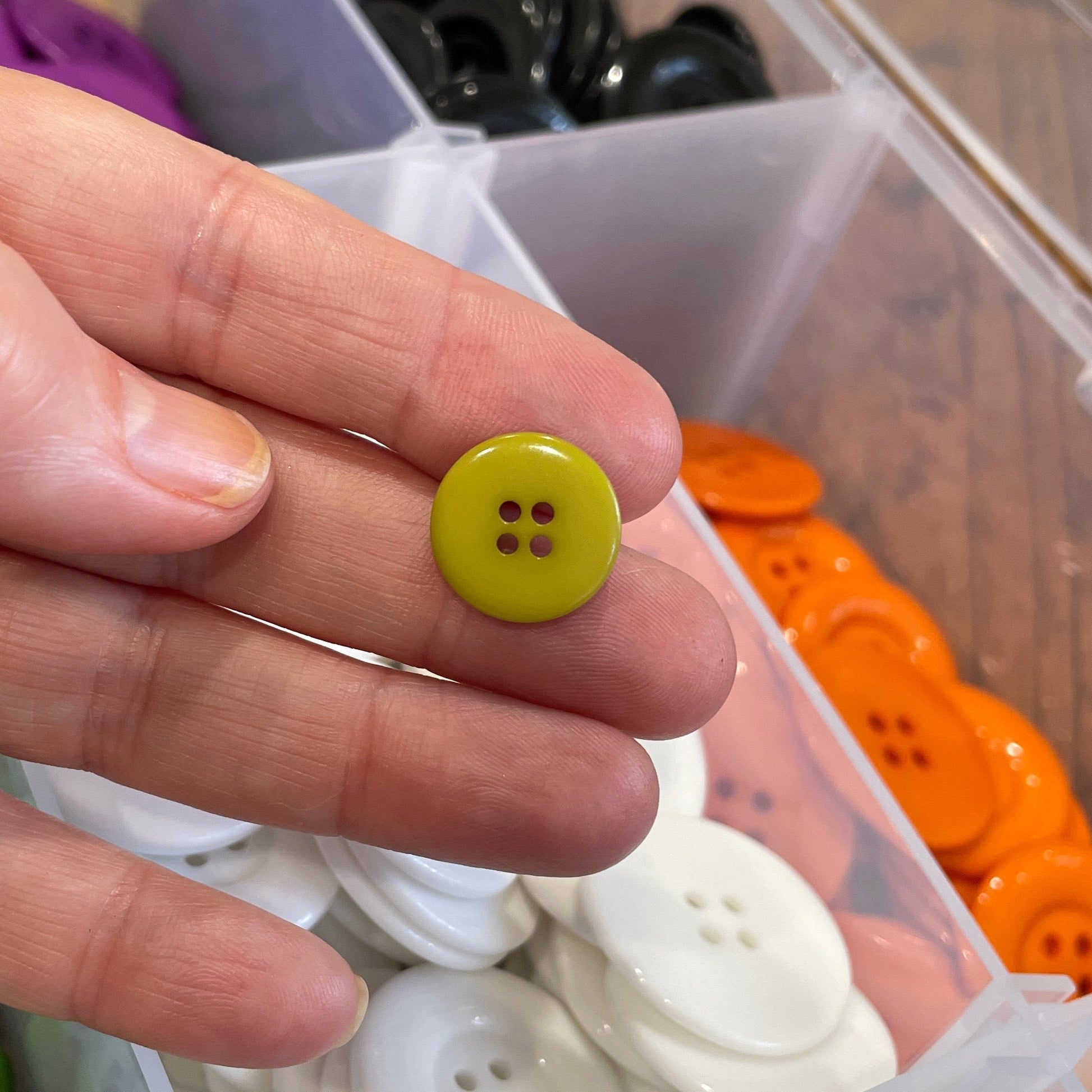 Hand holding a yellow button with a container of assorted buttons in the background