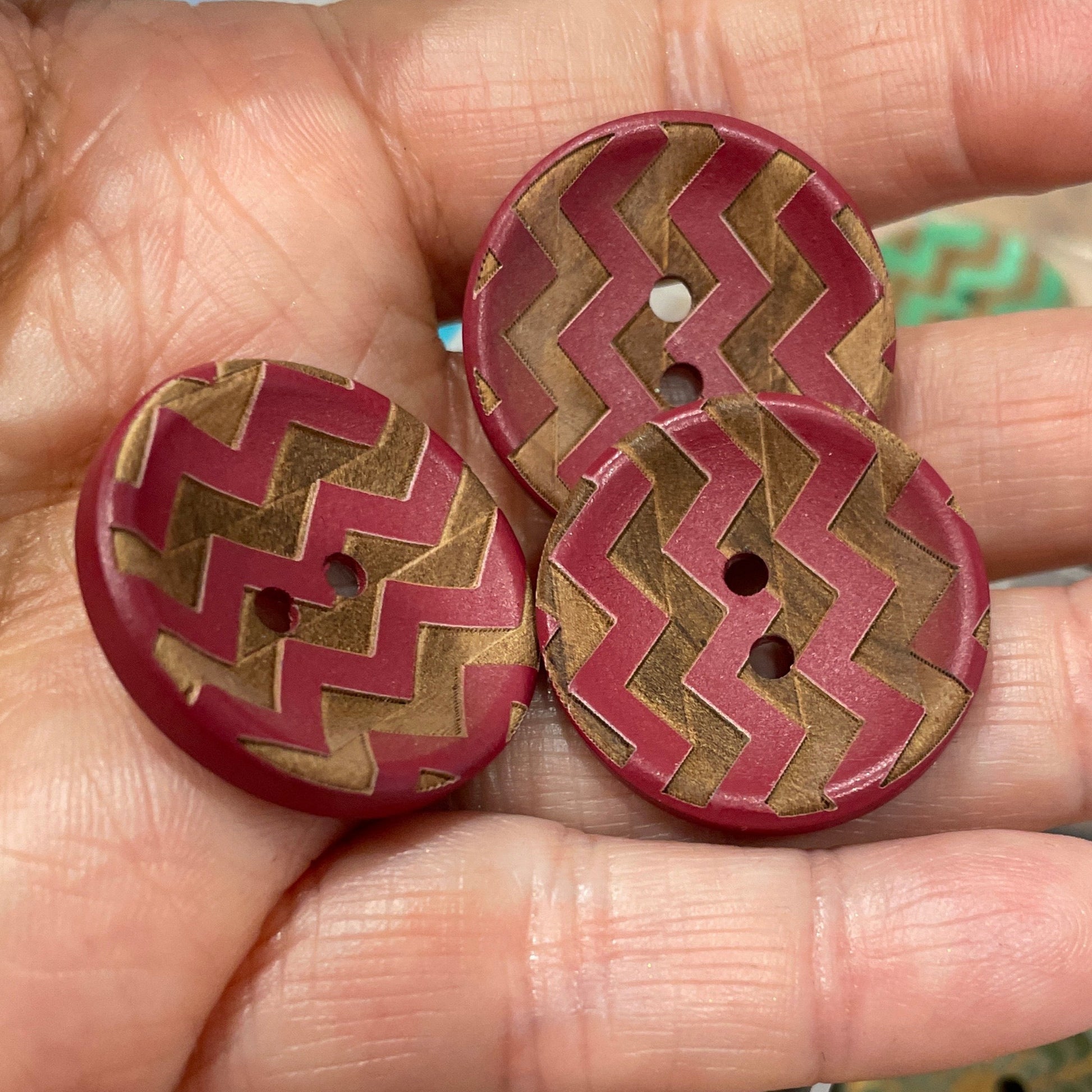 Hand holding three decorative buttons with a zigzag pattern, with a container of more buttons in the background.