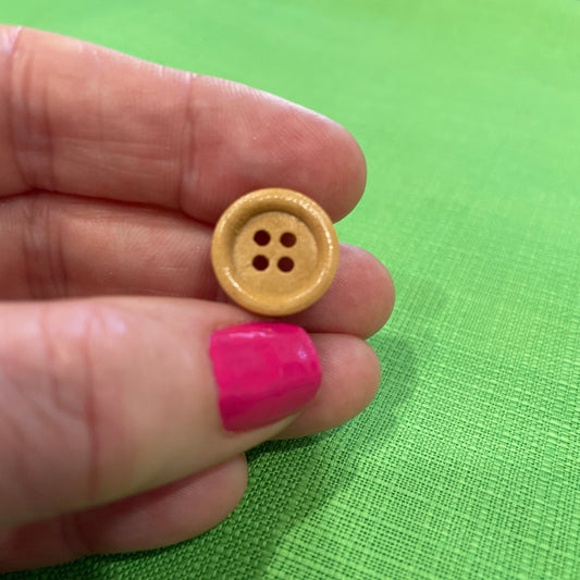 Hand holding a small gold button against a green background
