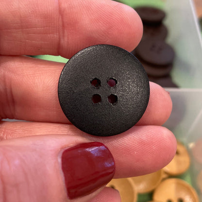 Black button held between fingers with a container of buttons in the background