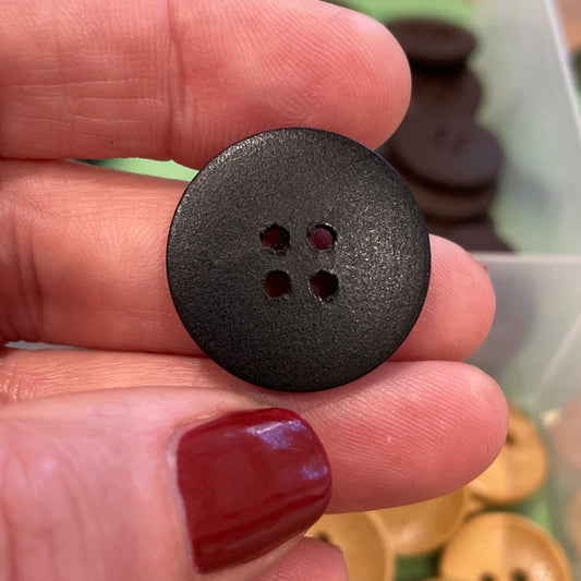 Black button held between fingers with a container of buttons in the background