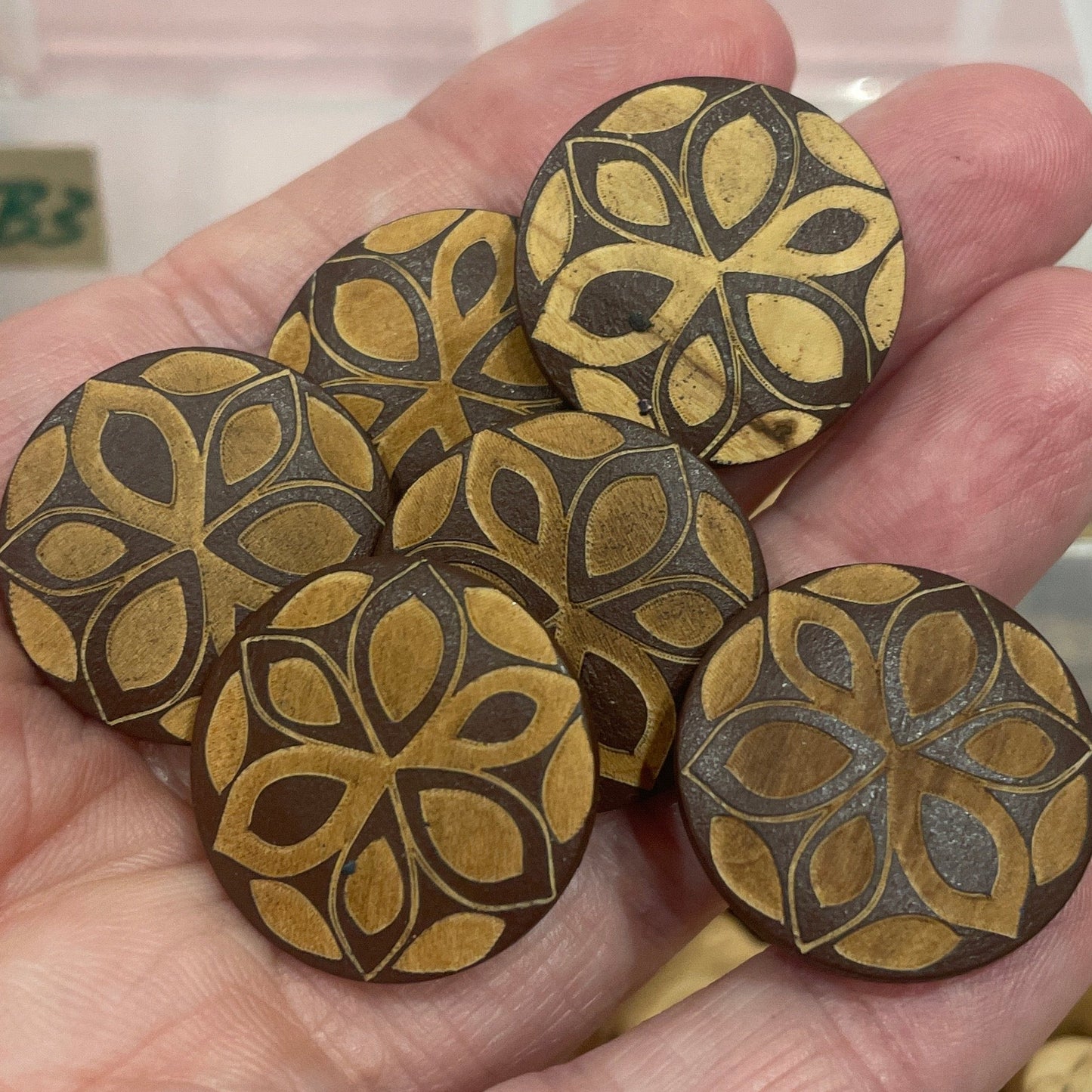 Hand holding decorative wooden buttons with a blurred background of more buttons.