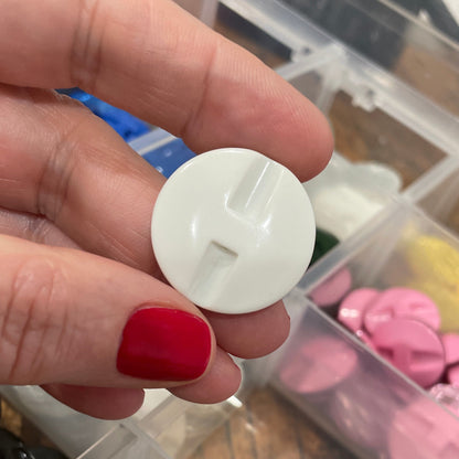 Hand holding a white button with a container of colorful buttons in the background