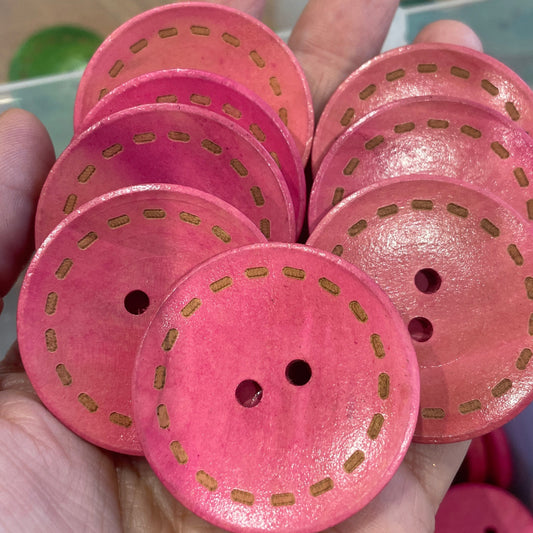 Pink buttons with gold accents held in a hand, with a blurred background of more buttons.