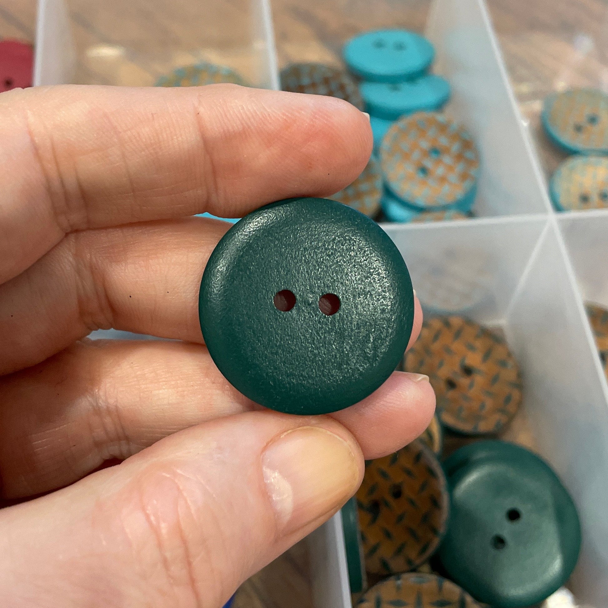 Hand holding a green button with a container of buttons in the background