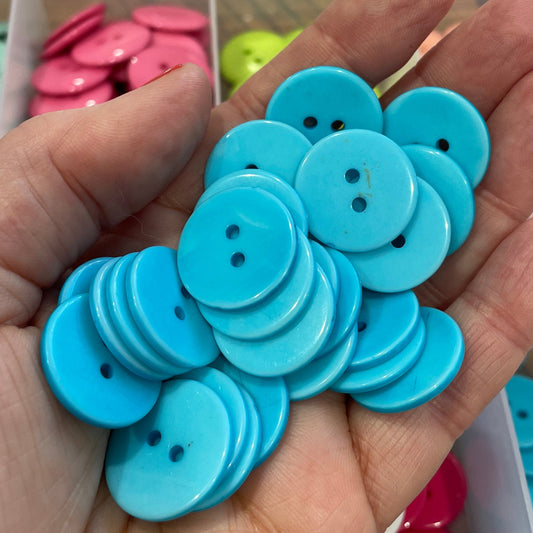 Hand holding blue buttons with a container of buttons in the background