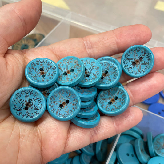 Hand holding blue buttons with decorative patterns, with a container of more buttons in the background.