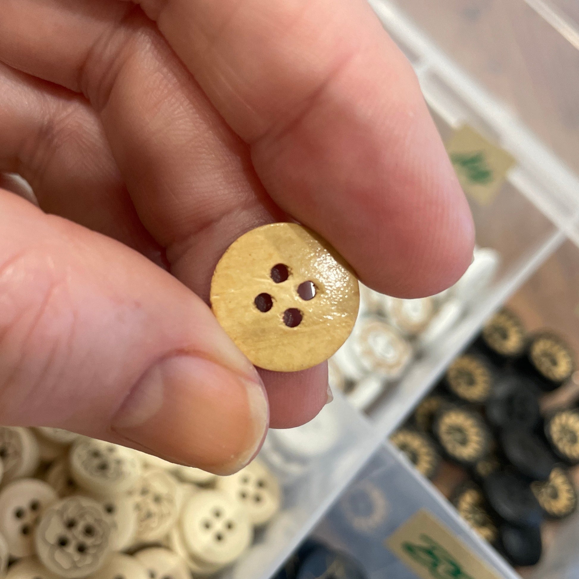 Hand holding a gold button with a container of buttons in the background