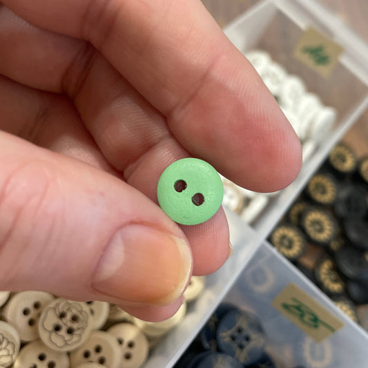 Hand holding a green button with a blurred background of button collection