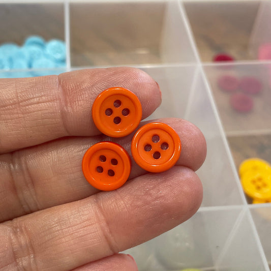 Hand holding two orange buttons with a background of colorful buttons in a container.
