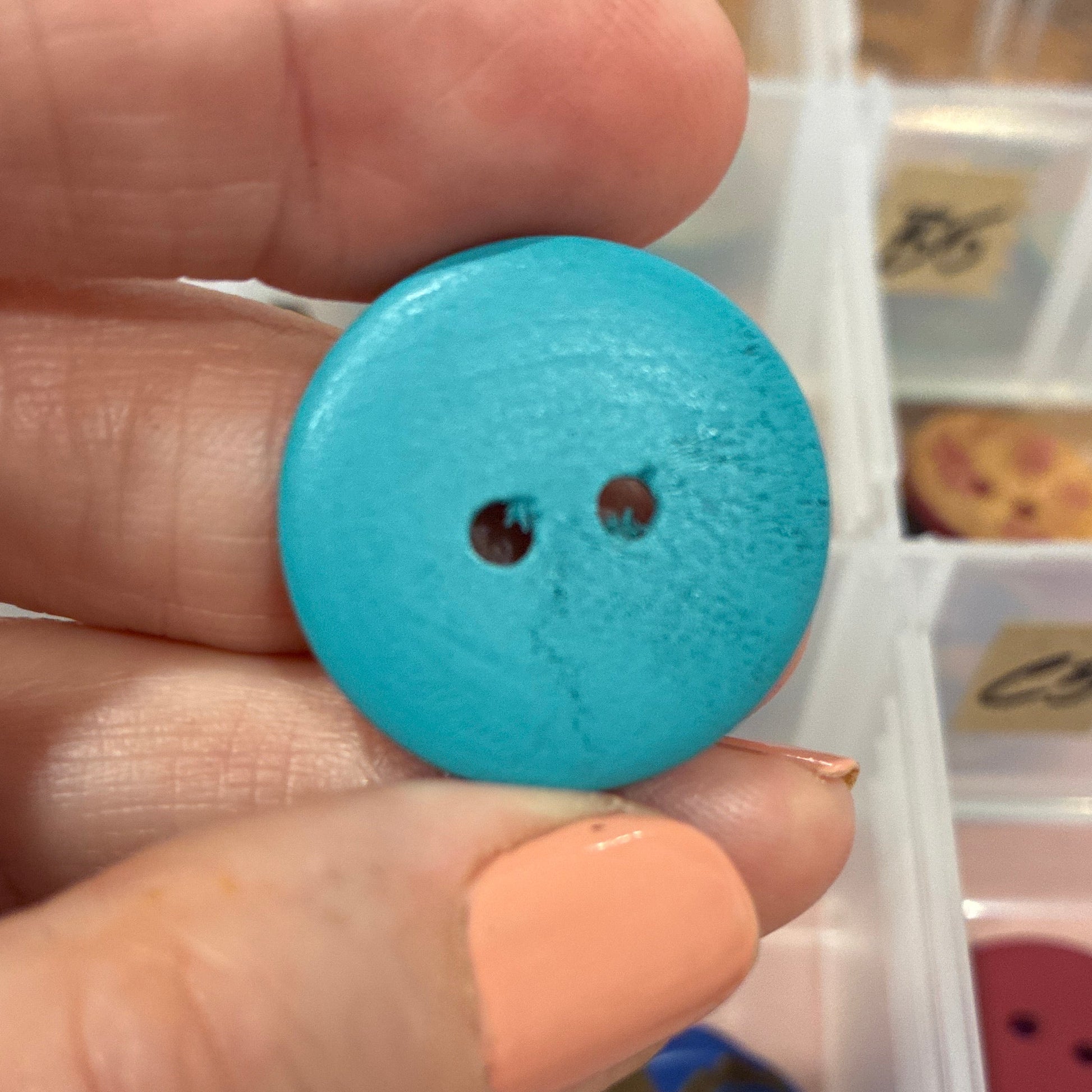 Hand holding a blue button with a container of buttons in the background