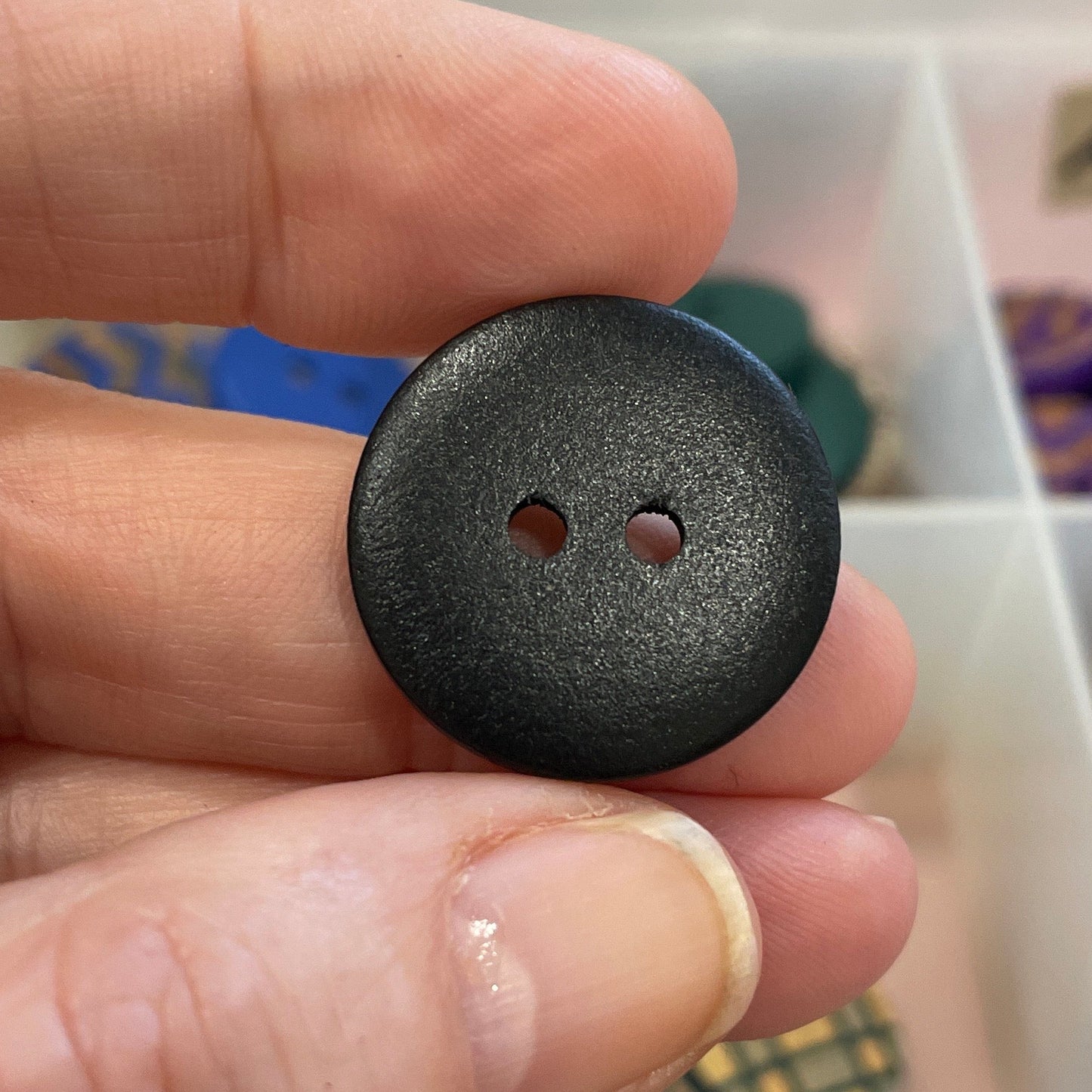 Black button held between fingers with a collection of buttons in the background