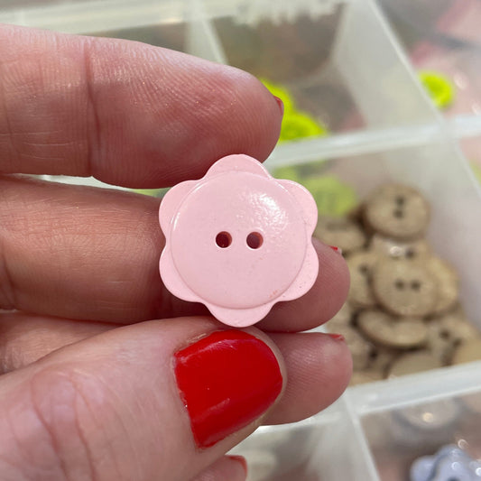 Hand holding a pink flower-shaped button with a blurred background of button collection
