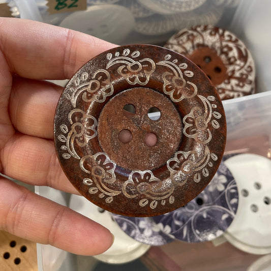 Decorative button held in a hand with a background of various buttons.