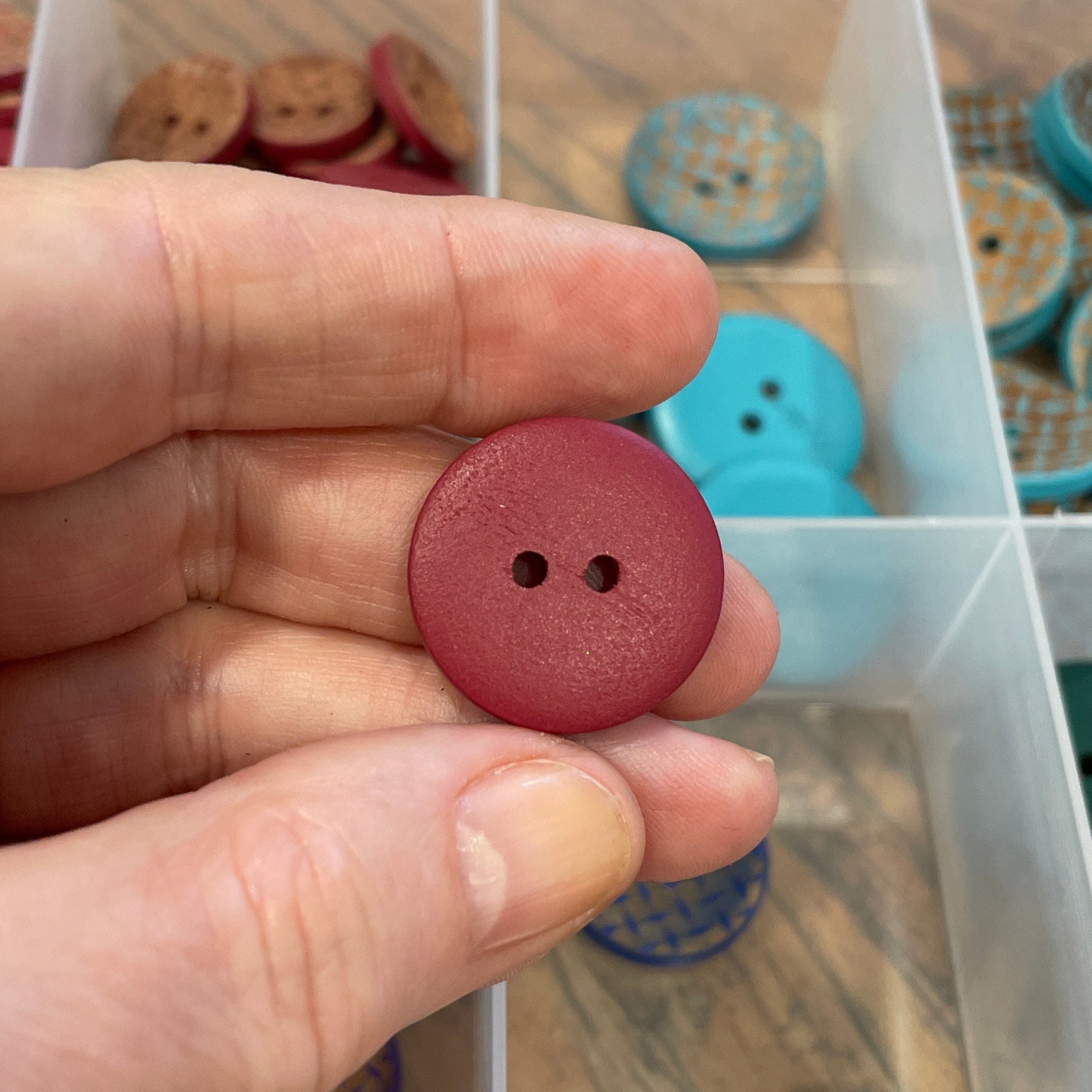 Hand holding a red button with a container of assorted buttons in the background