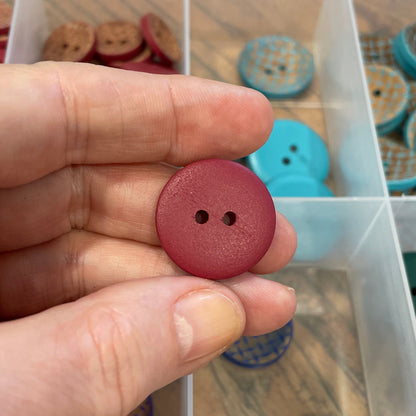 Hand holding a red button with a container of assorted buttons in the background