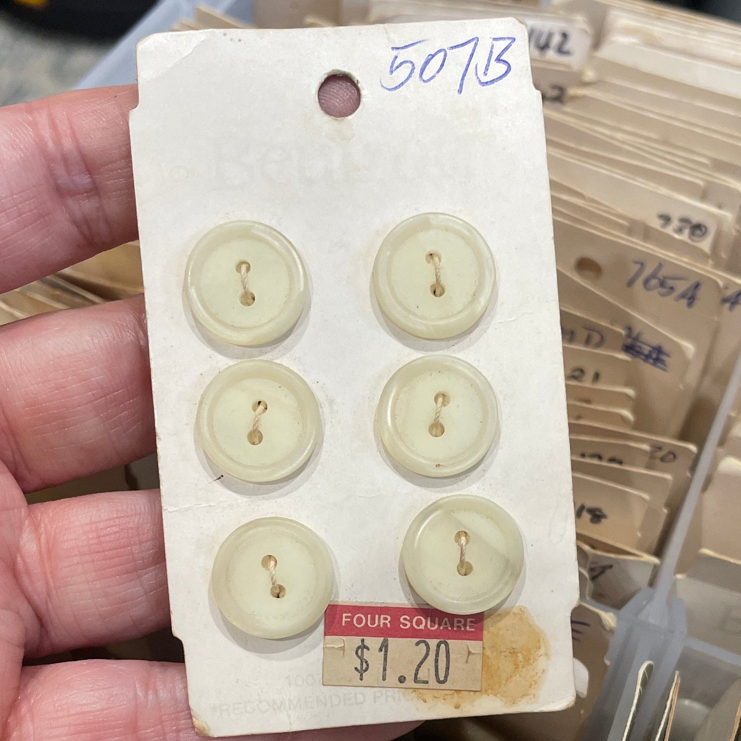 Hand holding a card with buttons in front of a container of similar items