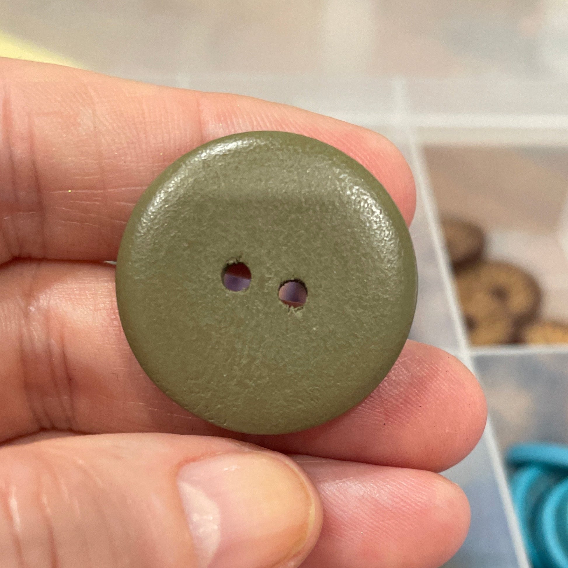 Hand holding a green button with a container of buttons in the background