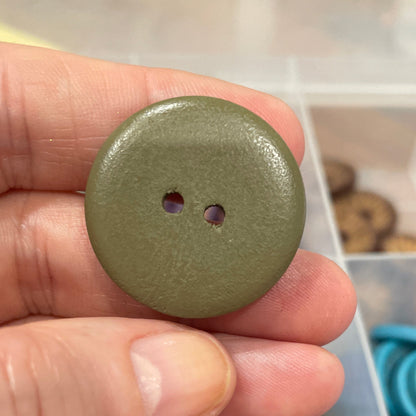 Hand holding a green button with a container of buttons in the background