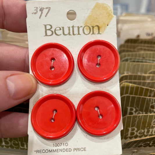Four red buttons on a Beutron card held by a hand with a blurred background