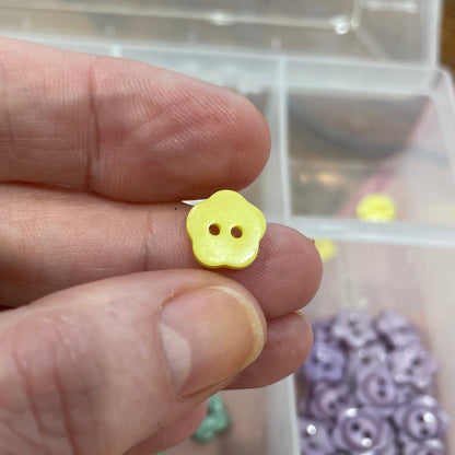 Hand holding a small yellow button with a clear container of buttons in the background