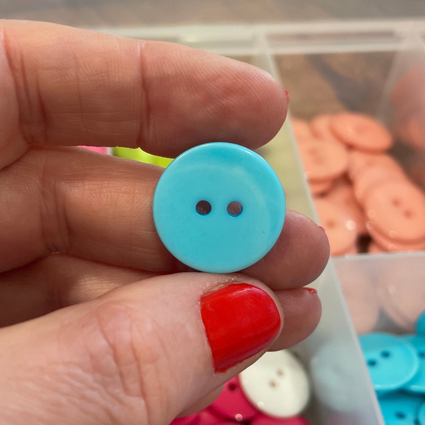Hand holding a blue button with a container of colorful buttons in the background