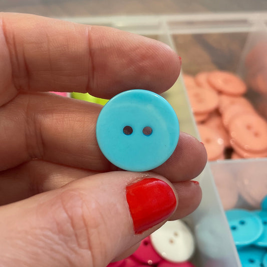 Hand holding a blue button with a container of colorful buttons in the background