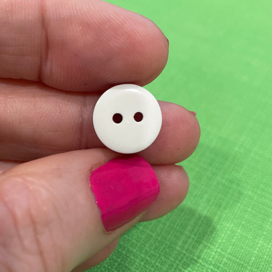 White button held between fingers against a green fabric background