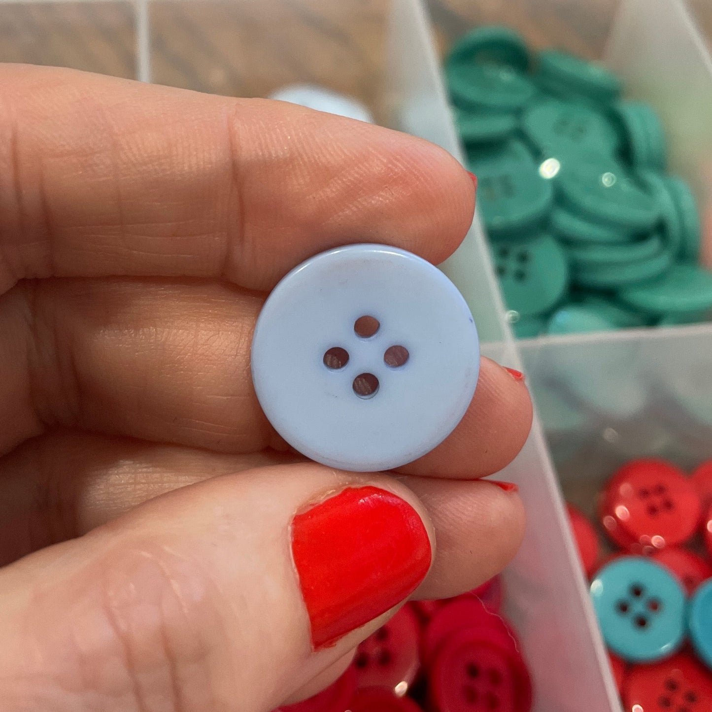 Hand holding a white button with a clear container of buttons in the background
