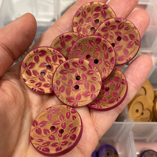 Hand holding floral-patterned buttons with a blurred background of button assortment.