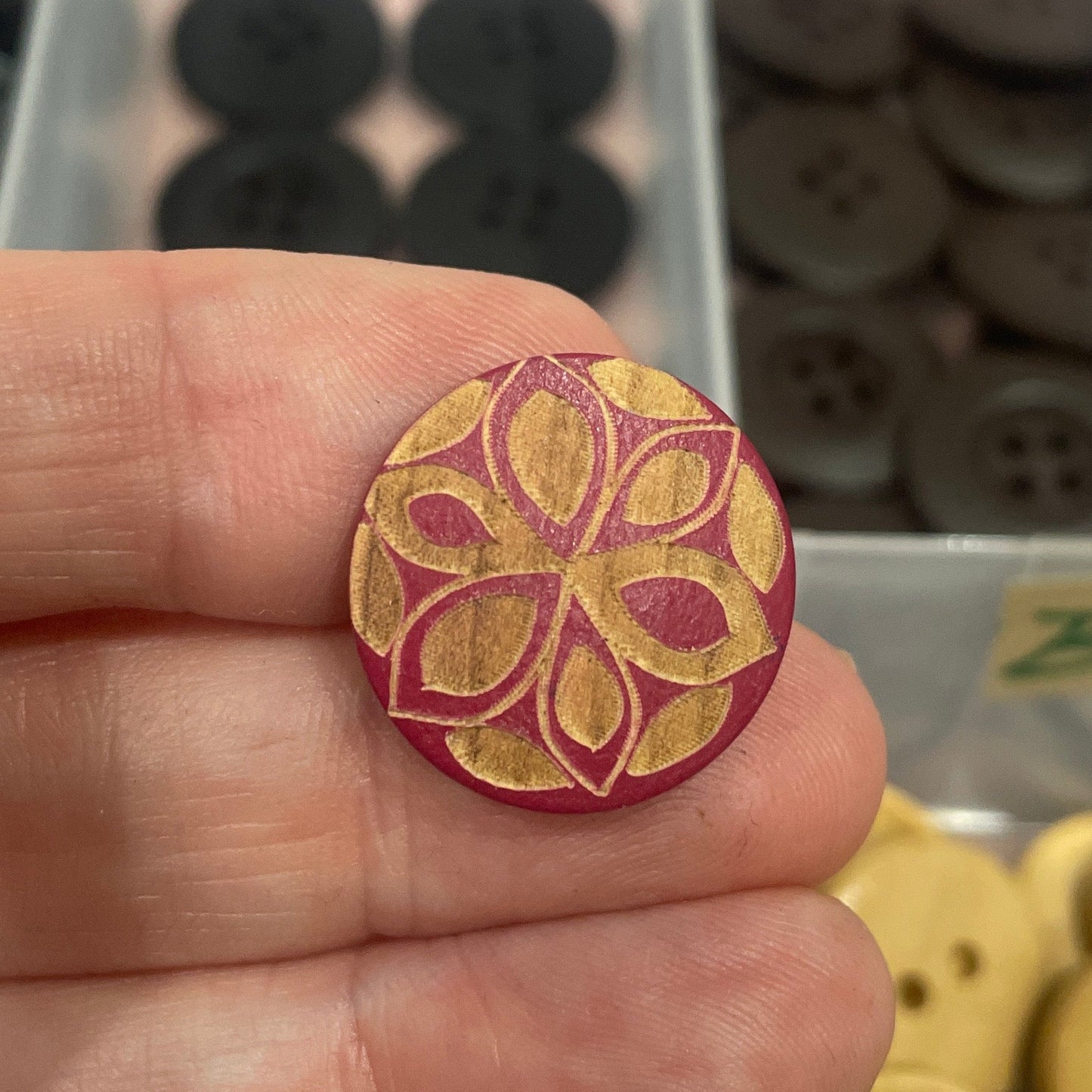 Hand holding a decorative button with a collection of buttons in the background.